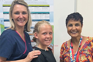 A young girl stands between two female audiologists