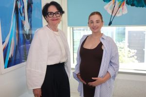 Peta Fisher and Christina standing together smiling, with some blue artwork in the background. 