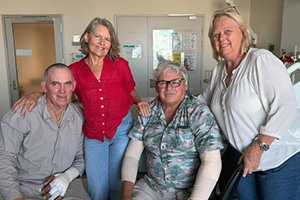 Two older women and two older men sit together. Both men have bandages on one or both of their hands or arms.
