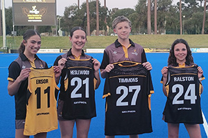 Four teenagers stand together holding their hockey jerseys in front of them