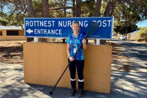 Clinical Nurse Specialist Cassie standing in front of the Rottnest Island Nursing Post sign, holding an oar. 