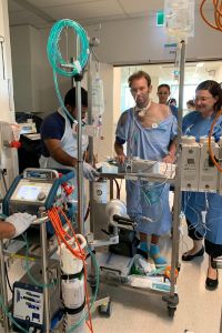 Clint walking down a hallway in the FSH ICU, hooked up to the ECMO machine.