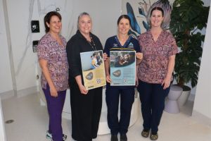 Four female clinicians standing together inside the FSH Family Birth Centre, with two of these clinicians each holding a poster.