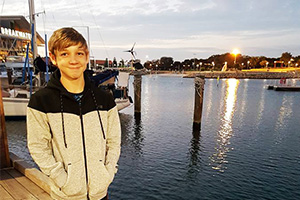A young boy stands on a jetty as the sun sets behind him