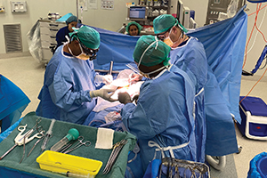 Three health professionals perform surgery on a patient in a theatre.