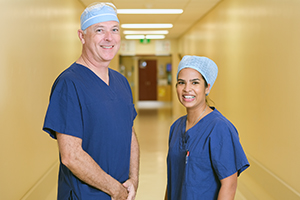 A male and female doctor wearing surgical scrubs and caps stand in a corridor.