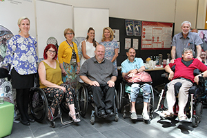 Four people in wheelchairs and another five people are in front of display boards and banners.