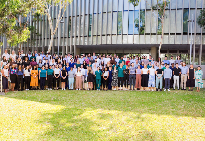 A group of 120 interns standing all together on grass, in front of a building.