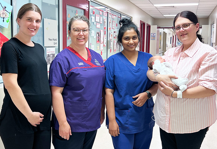 A pregnant woman, a midwife, a doctor and a woman holding a newborn baby stand side-by-side in a corridor