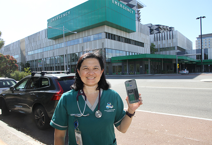 Emergency Medicine Consultant Simone Bartlett stands outside Fiona Stanley Hospital holding a smart phone in her left hand.