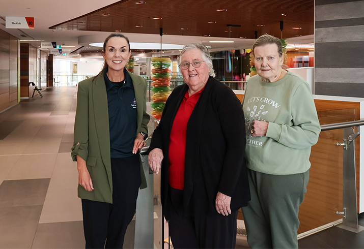 Senior Physiotherapist Caitlin Vicary standing on the left, with program participants Jenny and Kay standing to the right, in front of a bannister.