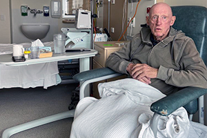 An older man sits in a high back chair in a hospital room