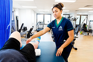 A female physio treats a patient whose legs can be seen laying on a treatment table.