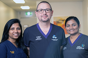 Two female and one male nurse stand together in a corridor