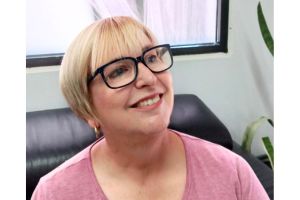 Kate wearing a pink shirt and black framed glasses, smiling looking into the distance.