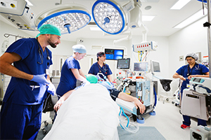 A team of health professionals care for a patient laying on a bed in an operating theatre