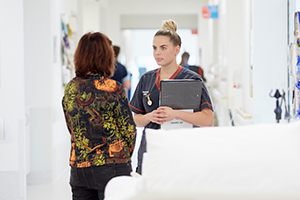 A female nurse talks to a person in a hospital corridor.