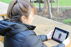 A woman seated outside watches a video on a tablet device. On the screen a pregnant woman sits on a fit ball.