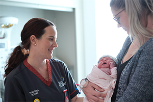 A midwife stands beside a woman who is holding a newborn baby.