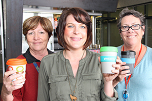 Three women stand holding environmentally sustainable 'keep cups'