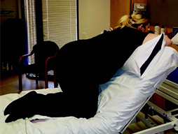 A pregnant woman kneels on a bed on which the bed head has been raised