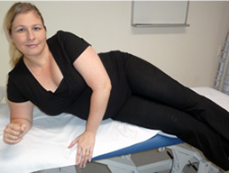 A woman moves to a standing position from a bed with her hands placed on her thighs.