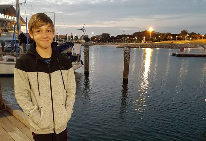 A young boy stands on a jetty as the sun sets behind him