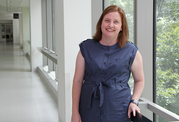 Dr Hayley Robinson leans against a balustrade next to a floor length window