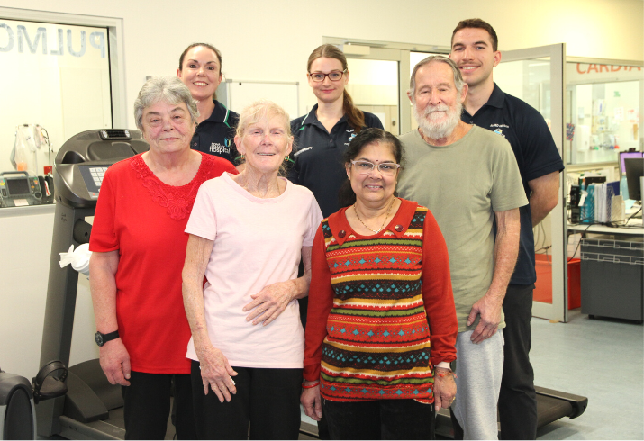 Four pulmonary rehabilitation patients and three staff standing together in the gym smiling.