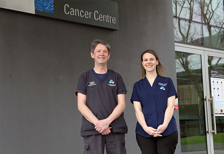 A man and a woman stand outside a building underneath a sign that reads Cancer Centre