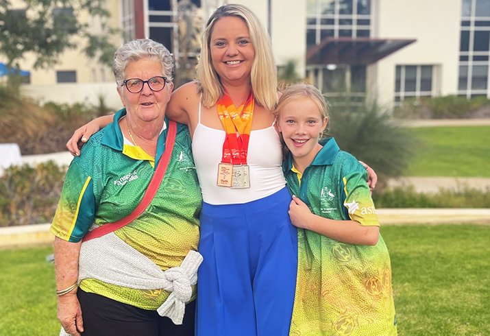 A woman wearing multiple winners medals stand between an older woman and a teenage girl in a garden setting