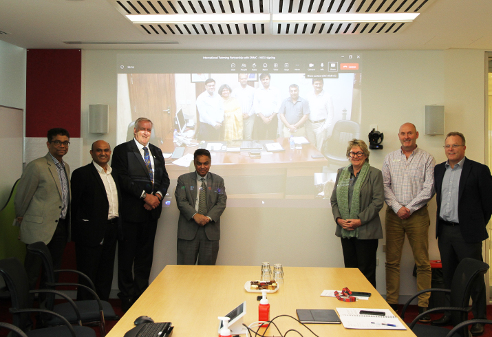 Representatives from SMHS and Perth Consulate General of India stand together in front a video call with the Sarojini Naidu Medical College.