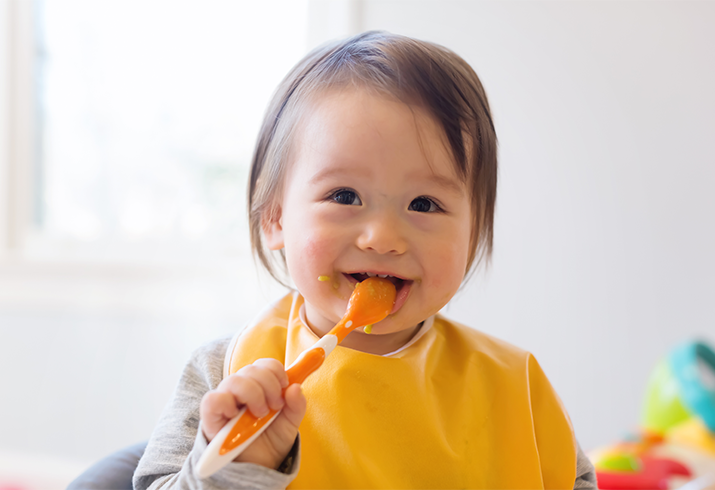 Baby places spoon in mouth and smiles