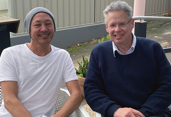 Two men sit on outdoor furniture in an outdoor area