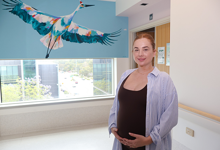 Christina pictured at 28 weeks pregnant, standing at the end of a hallway with her hands on her belly.