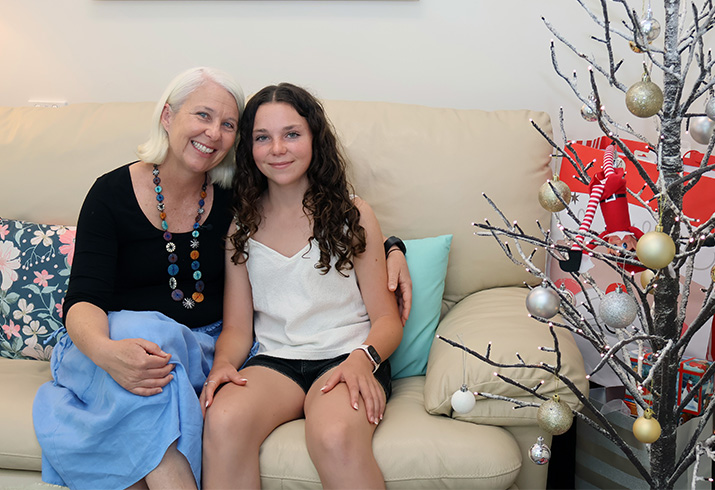 Abby Ralston (right) sits on a couch next to her mum. A Christmas tree stands to the left of the couch.