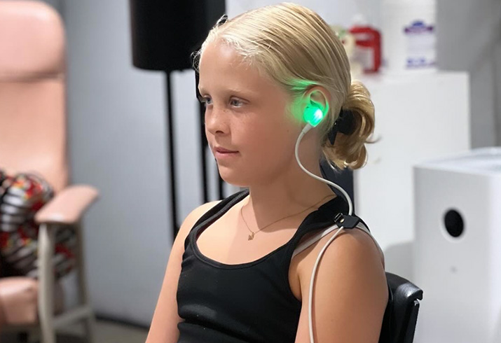 A young girl sits with a monitor inserted in her left ear during an audiology assessment