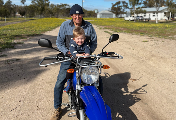 Clinical trial participant Paul sits on a motorbike with his grandson.