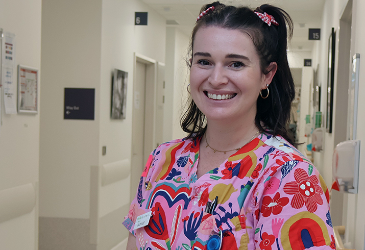 Fiona Stanley Hospital Clinical Midwife Bronywn stands in a hallway wearing bright scrubs.