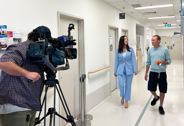 Clint pictured on the far right walking down a hallway with a Channel 9 journalist, with a cameraman in the foreground.