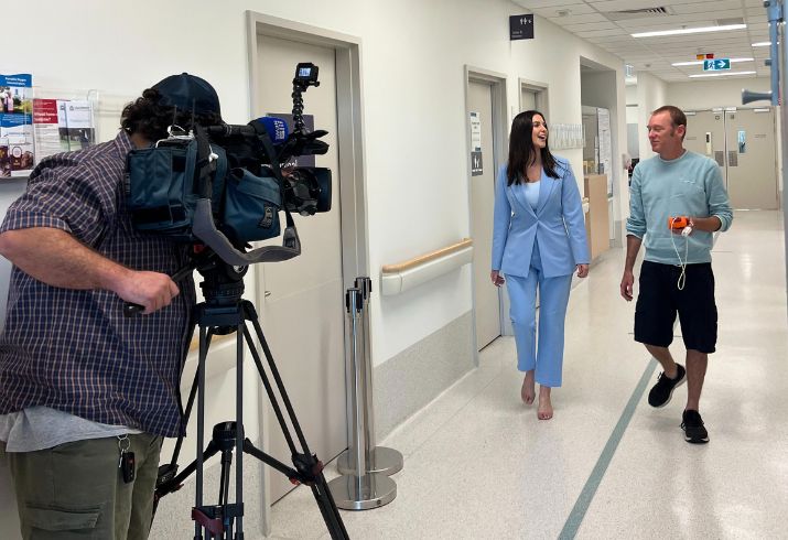 Clint pictured on the far right walking down a hallway with a Channel 9 journalist, with a cameraman in the foreground. 