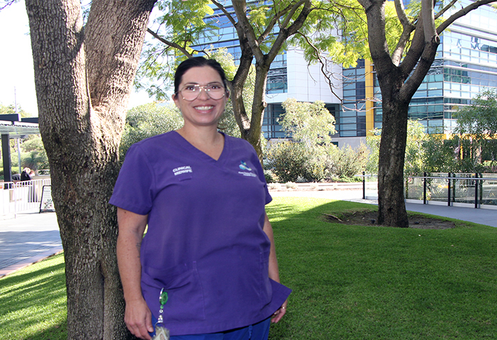 An endorsed midwife wearing purple scrubs stands in a garden at Fiona Stanley Hospital