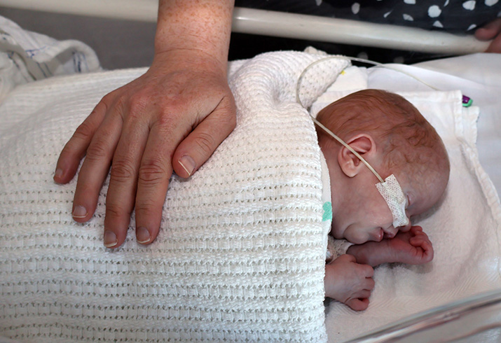 A woman's hands lays across the back of a small newborn baby laying in a crib