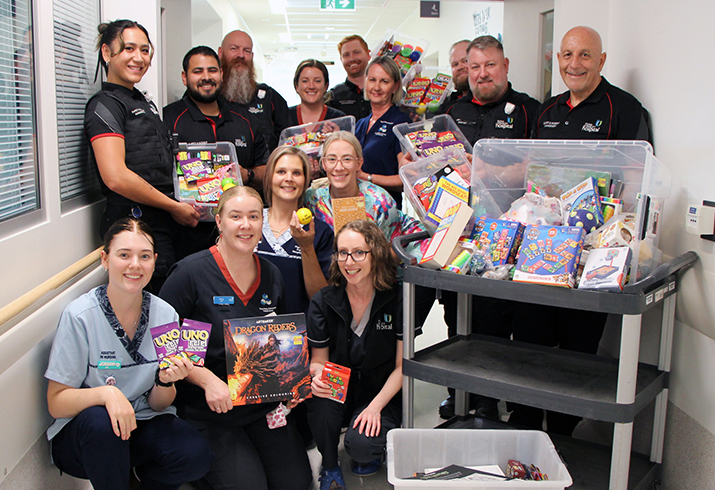 A large group of Fiona Stanley Hospital nursing and security staff stand around tubs filled with books and puzzles.