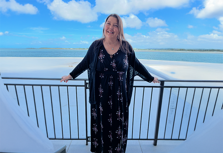 A stands on a balcony with the ocean behind her.