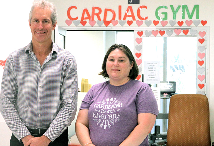 Professor Andrew Maiorana stands next to patient Sarah. Behind them on a wall are the words Cardiac Gym