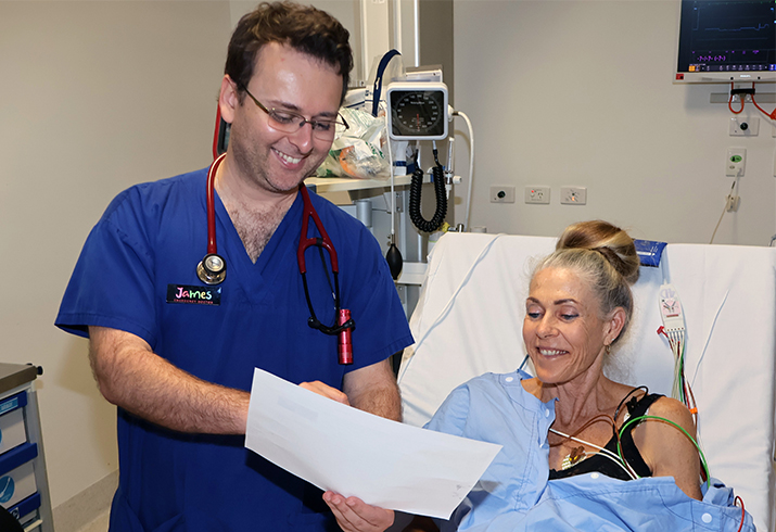 A male emergency doctor stands beside a woman who is laying in a hospital bed connected to monitoring equipment.
