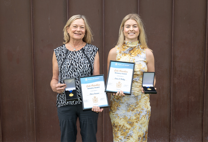 Claire and Emma standing side by side each holding a framed certificate and gold medallion.